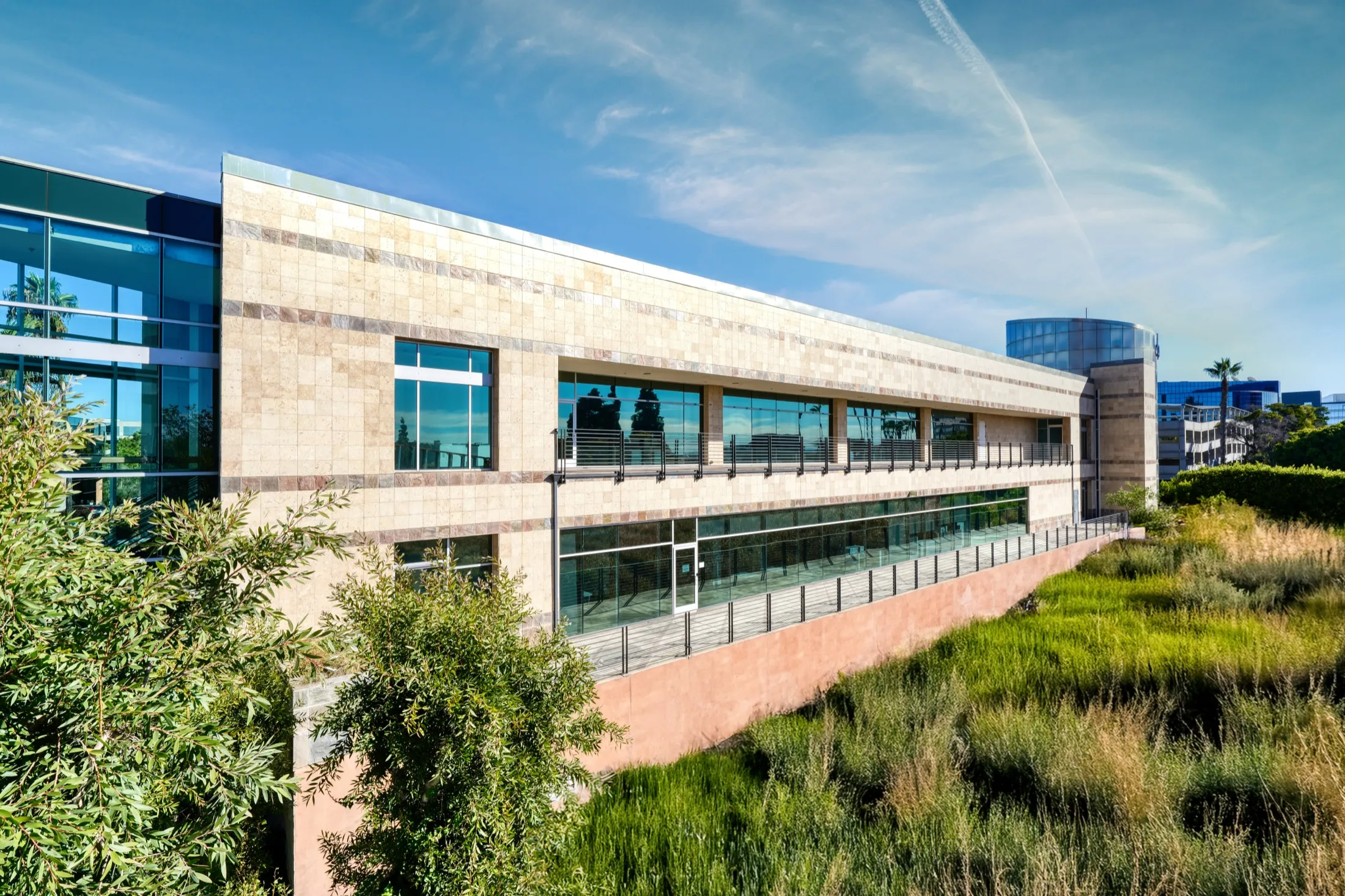 The long stone-and-glass side of 4475 Executive Drive, San Diego, above native planting