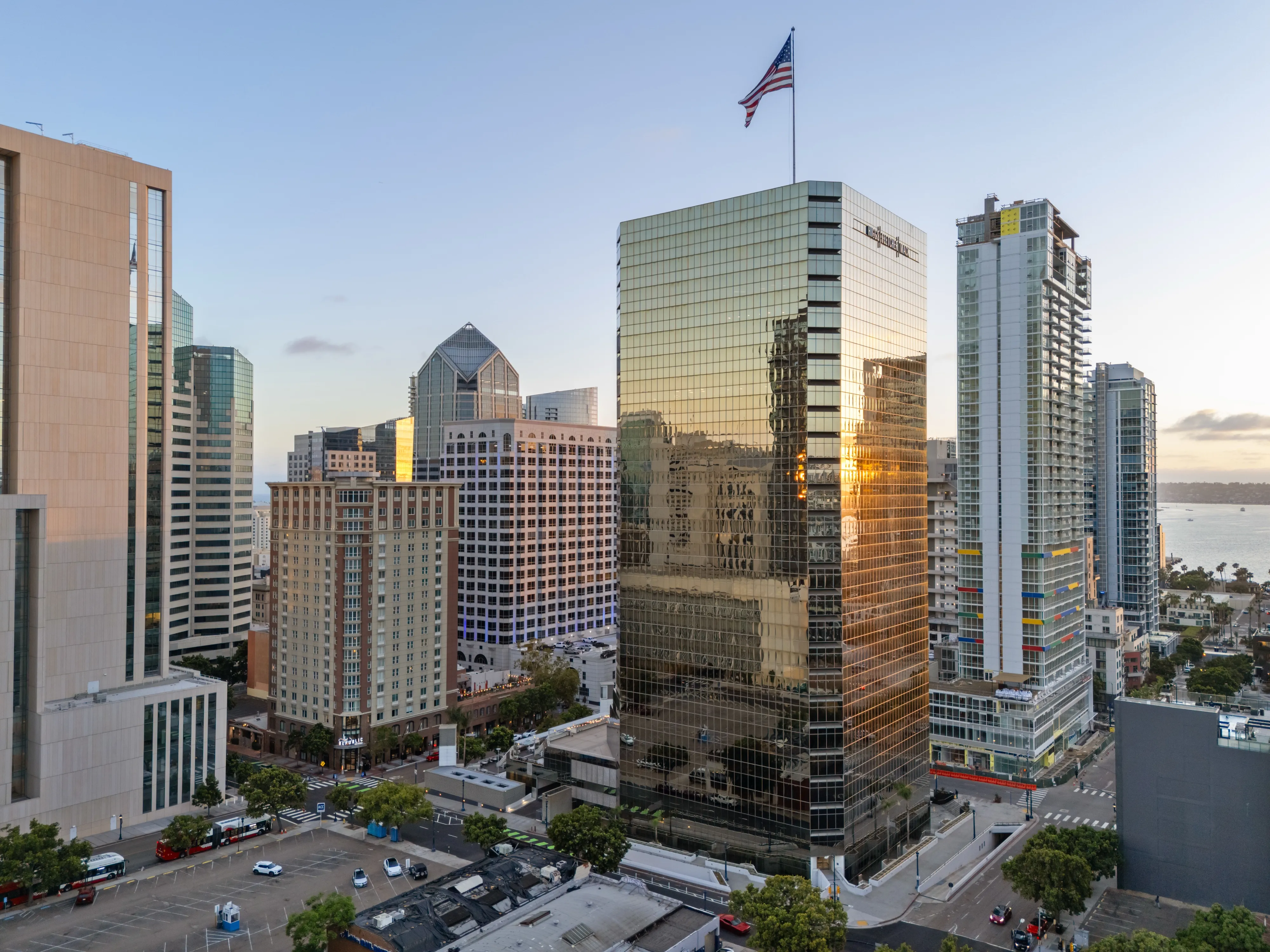 1 Columbia Place at golden hour from the air, the glass tower lit from the west with San Diego Bay behind