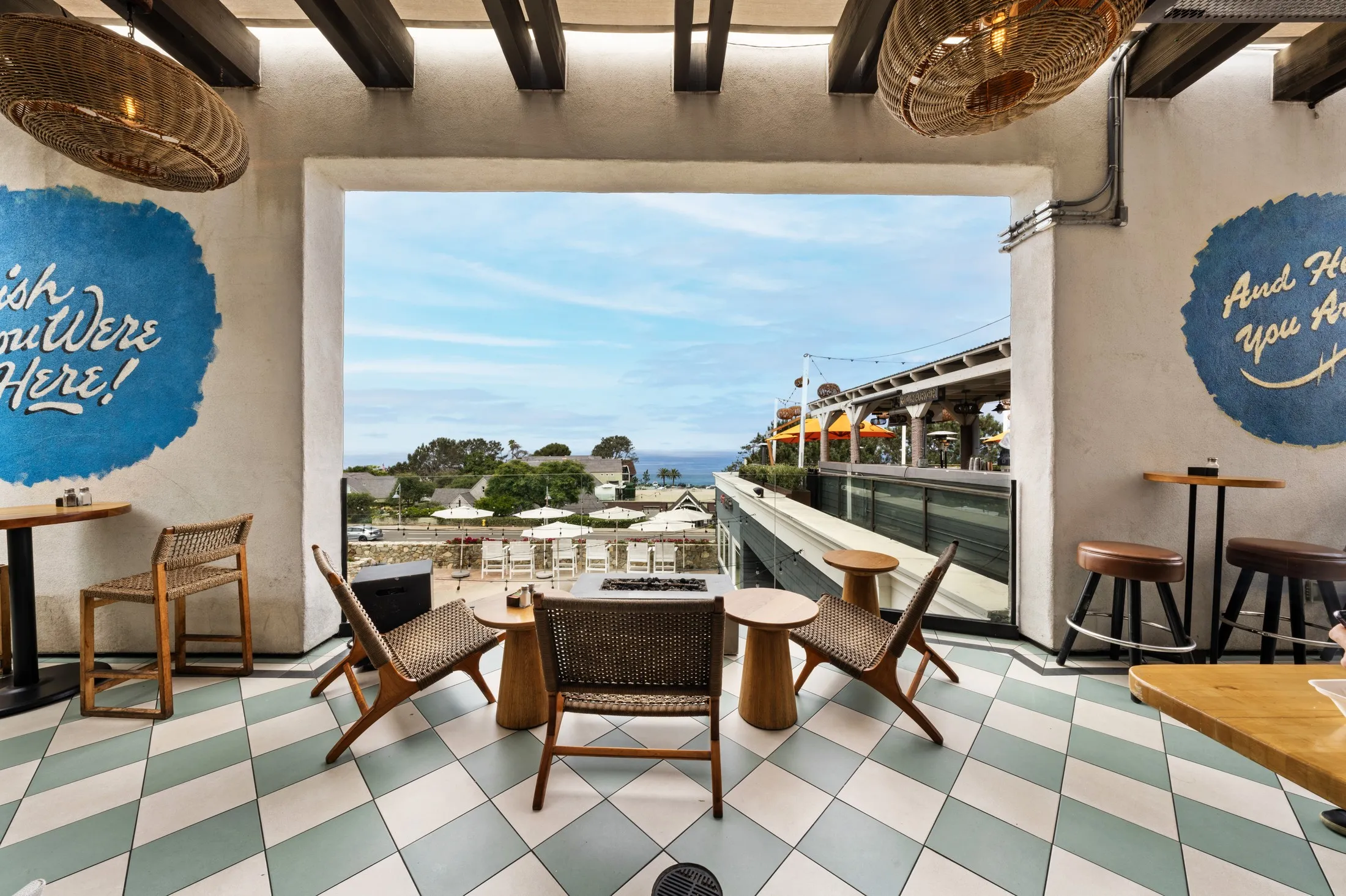 Rooftop terrace at Del Mar Plaza framed by a stone archway, checkerboard tile floor and an ocean view beyond