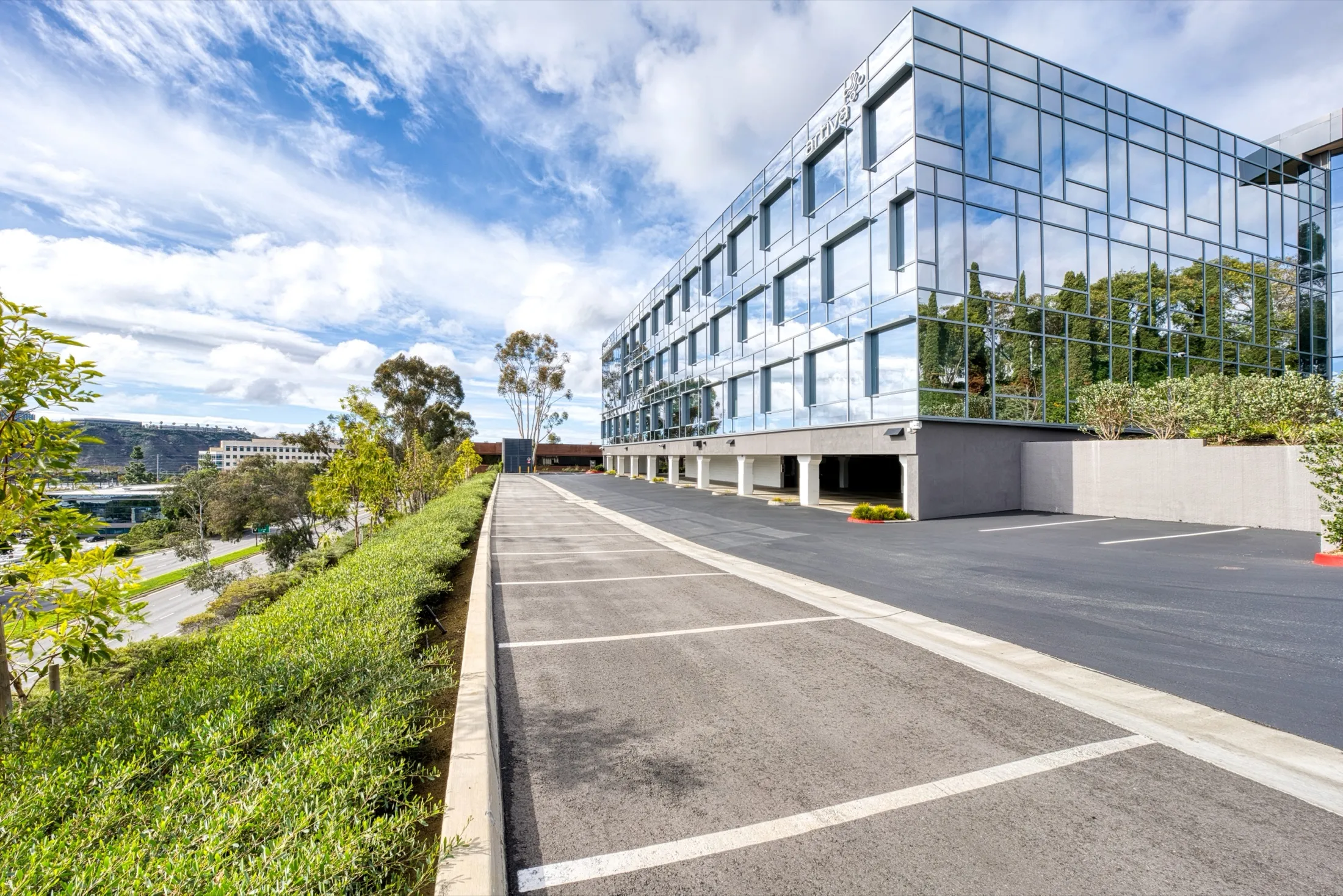 Ground view of 5505 Morehouse Drive's glass front from the parking deck, a planted slope alongside.