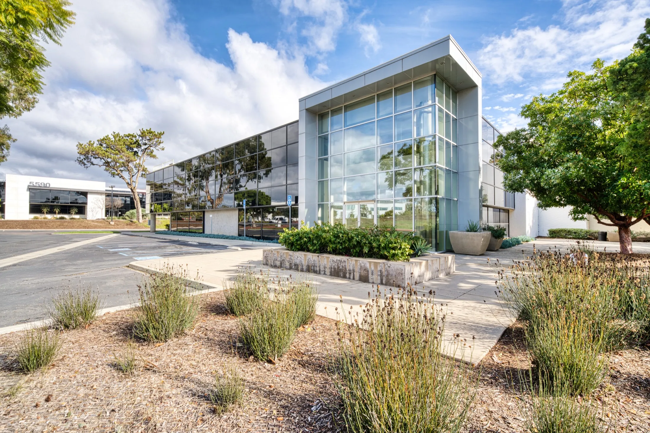 Ground view of 5550 Morehouse Drive's two-story glass entry on the corner, drought planting in front.